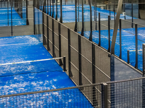 Overzicht van meerdere blauwe padelbanen bij Dekker Zoetermeer, omringd door glazen wanden en hekwerk, klaar voor een sportief potje padel.