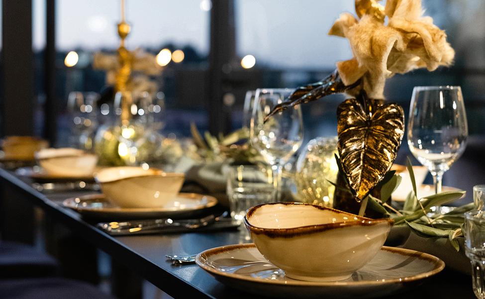 Sfeervol gedekte dinertafel bij Dekker Warmond met wijnglazen, stijlvol servies, gouden bloemendecoratie en warme verlichting voor een feestelijk diner.