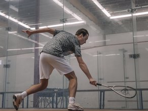 Squashspeler in actie op een indoor squashbaan bij Dekker Warmond, terwijl hij met zijn racket een lage bal probeert te slaan.