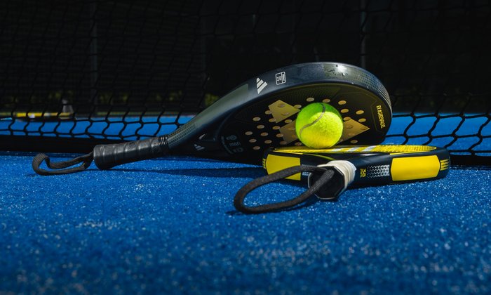 Twee padelrackets en een padelbal op een blauwe padelbaan bij Dekker Warmond
