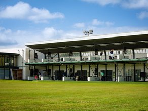 Driving range bij Dekker Warmond met twee verdiepingen en overdekte afslagplaatsen, waar golfers hun slag oefenen met uitzicht op het groene golfterrein.