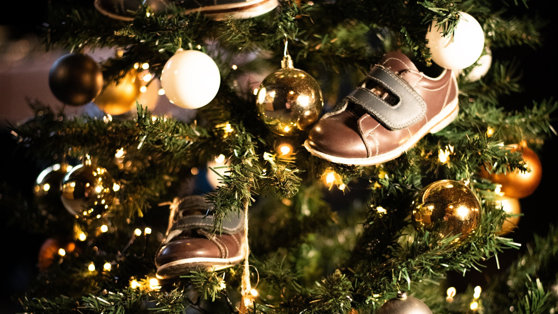 Close-up van een sfeervolle kerstboom bij Dekker Warmond met kleine kinderschoenen, gouden en witte kerstballen en warme kerstverlichting.