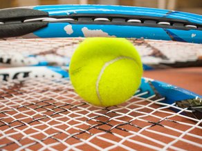 Close-up van een gele tennisbal tussen blauwe tennisrackets op een tennisbaan.