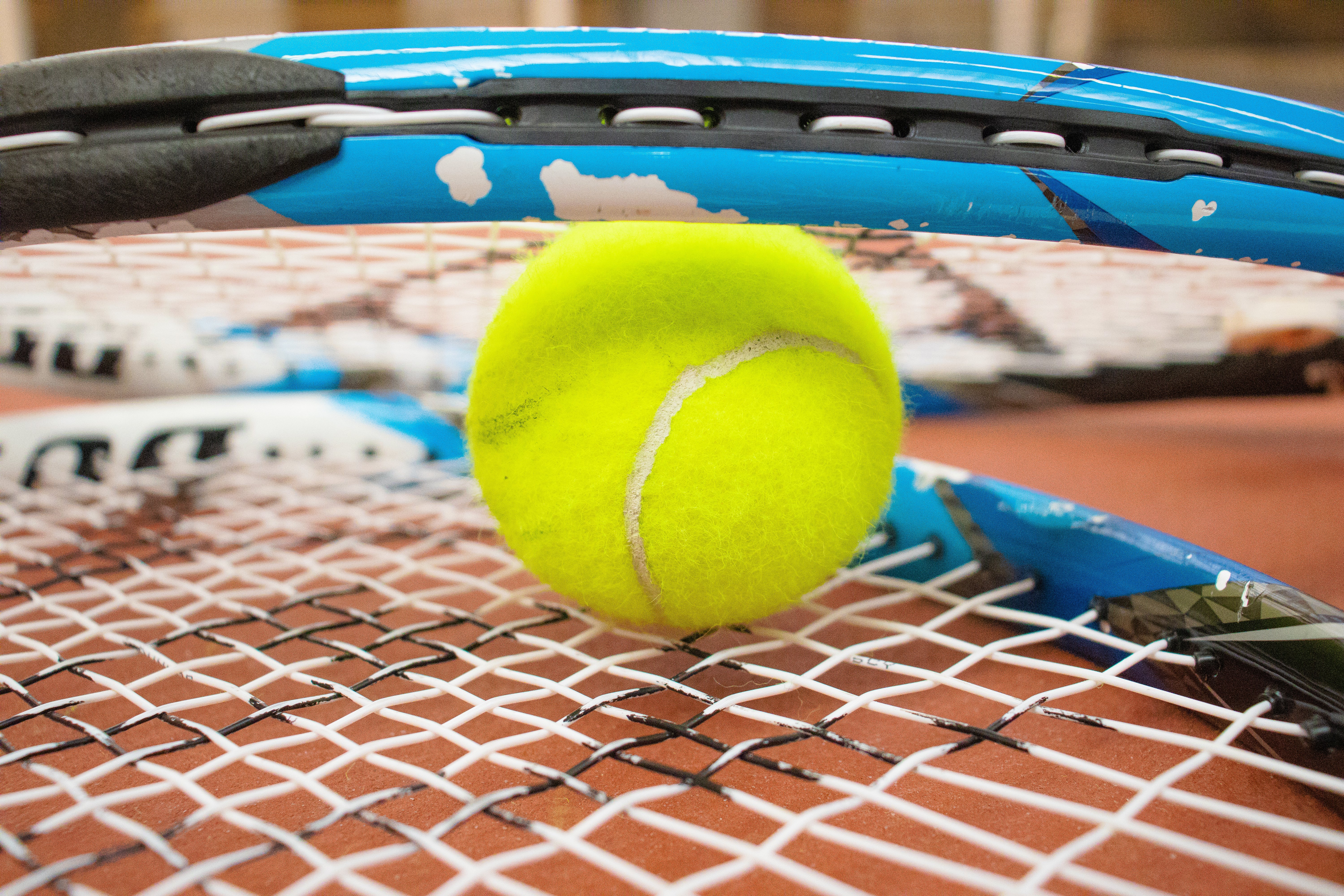 Close-up van een gele tennisbal tussen blauwe tennisrackets op een tennisbaan.