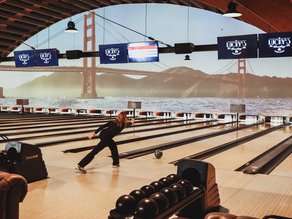Een vrouw gooit een bowlingbal op een van de bowlingbanen bij Lucky’s Bowling in Dekker Zoetermeer, met een grote afbeelding van de Golden Gate Bridge op de achtergrond.
