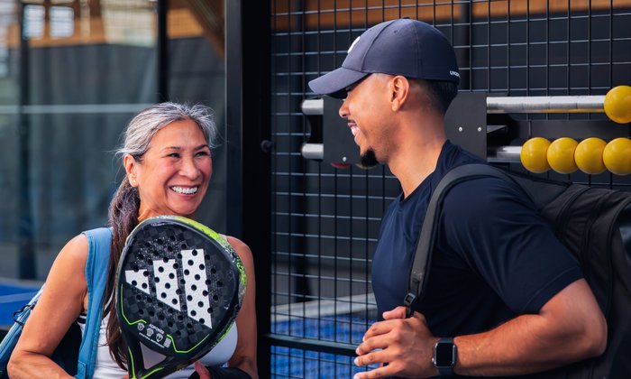 Twee lachende padelspelers met hun rackets bij de banen van Dekker Warmond