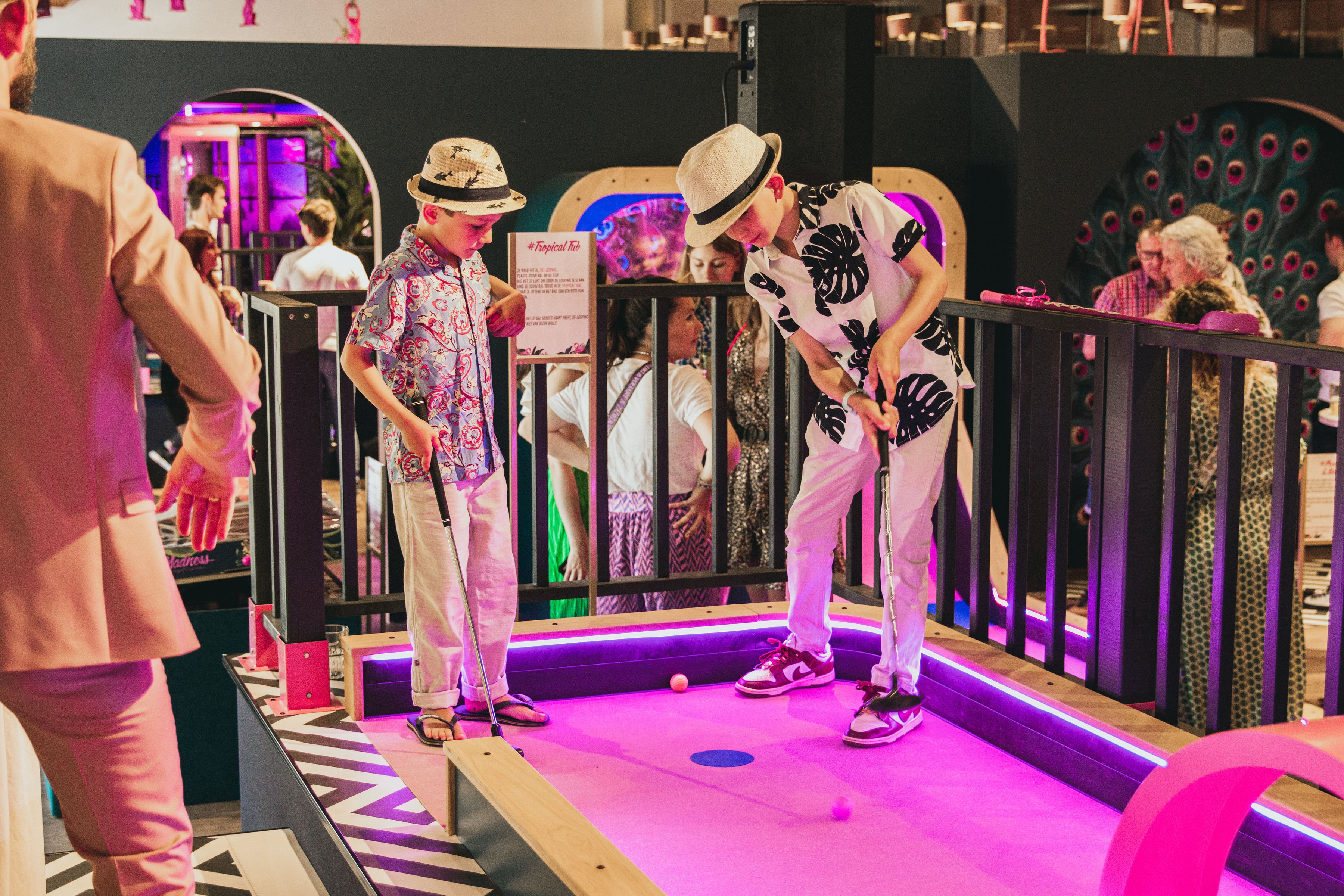Twee jongens spelen samen minigolf op een roze verlichte baan tijdens een feestelijk evenement bij Dekker Zoetermeer.