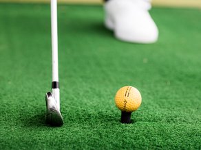 Close-up van een gele golfbal op een tee naast een golfclub op de driving range bij Dekker Warmond.