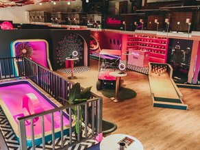 Overzicht van de Madness Minigolf Experience bij Dekker Warmond, met kleurrijke minigolfbanen, een roze golfkar, een candyshop en sfeervolle roze neonverlichting.