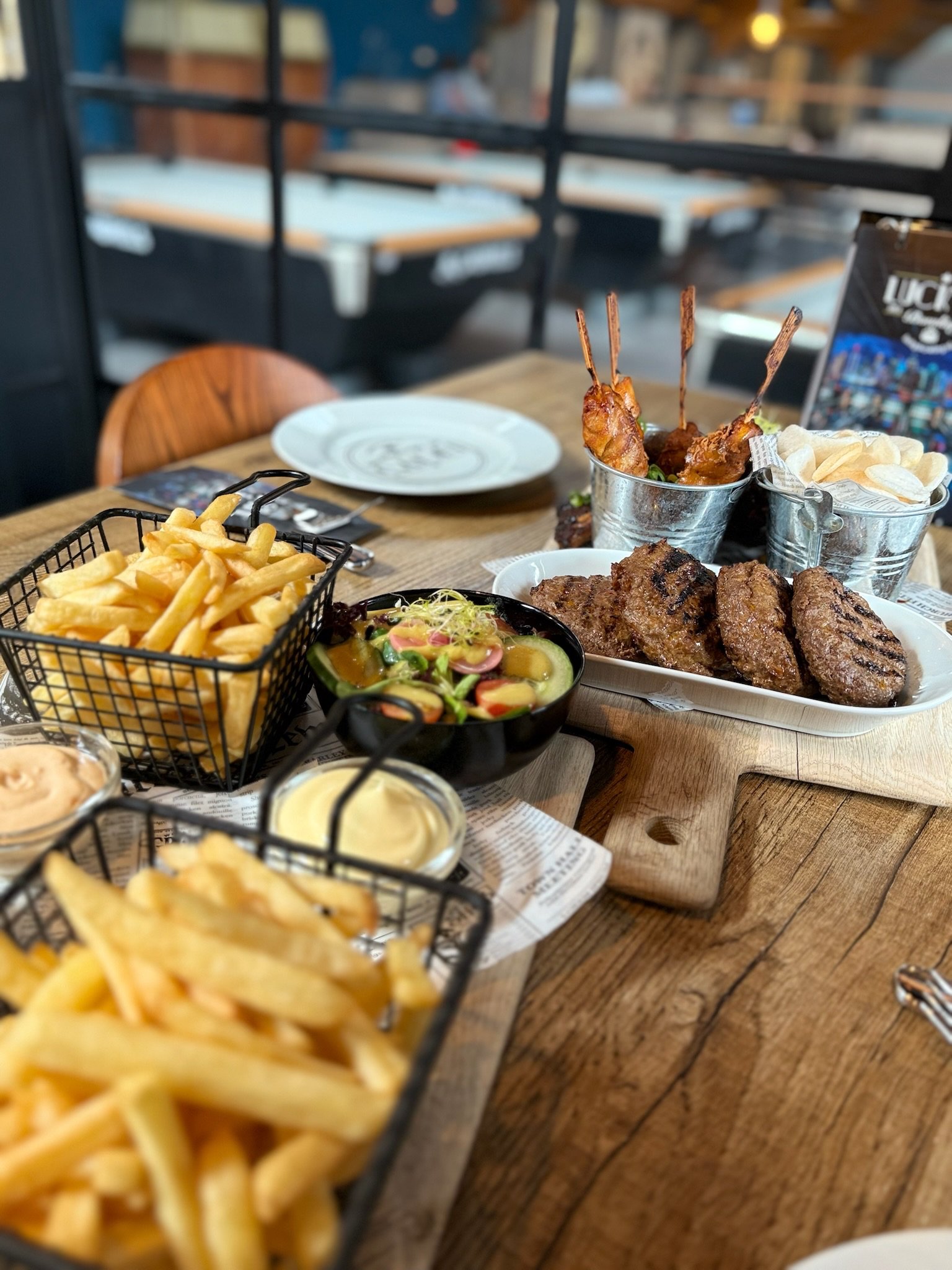 Een tafel vol heerlijke gerechten bij Dekker Warmond, met gegrild vlees, kipspiesjes, knapperige friet, salade en verschillende sauzen.