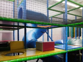 Kleurrijke indoor speeltuin bij Dekker Warmond met klimtoestellen, speelnetten, zachte speelelementen en een blauwe glijbaan voor kinderen.